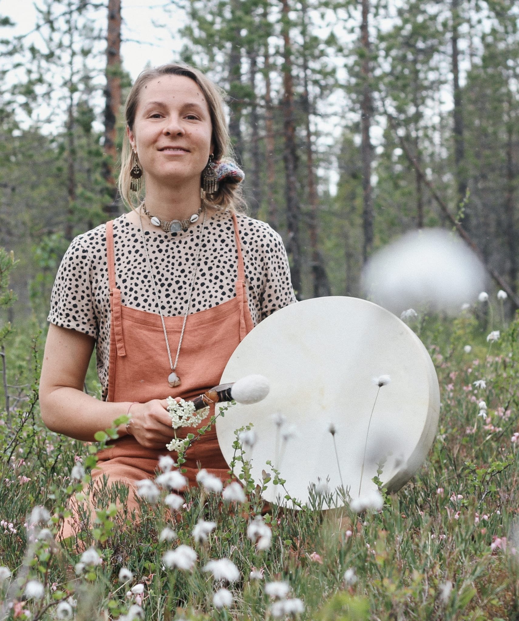 A woman sitting in a field of white flowers holding a large white gong and a mallet.