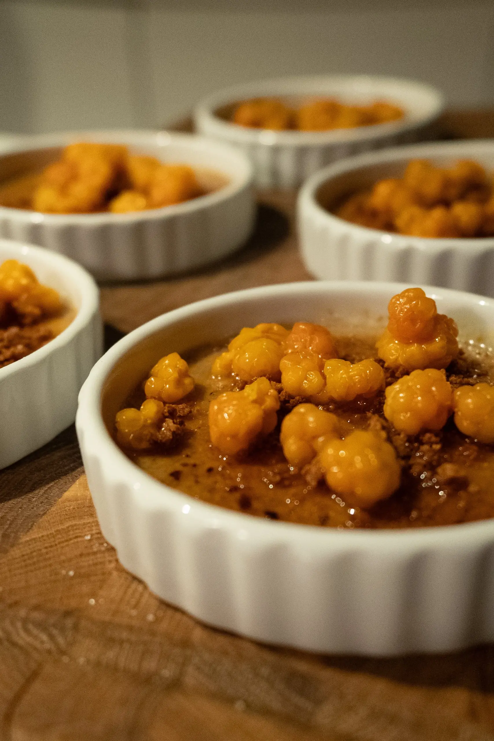 Multiple ramekins filled with a dessert topped with yellow berries, set on a wooden surface.