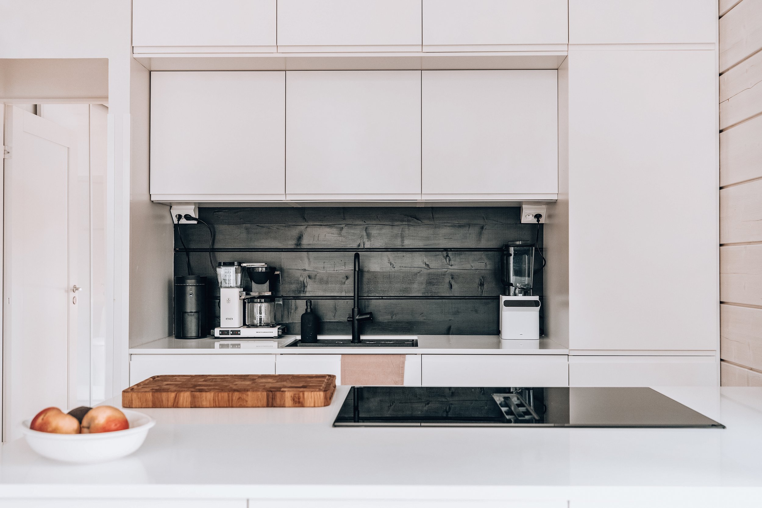 Modern minimalist kitchen with white cabinetry, black backsplash, and various small appliances on the countertop